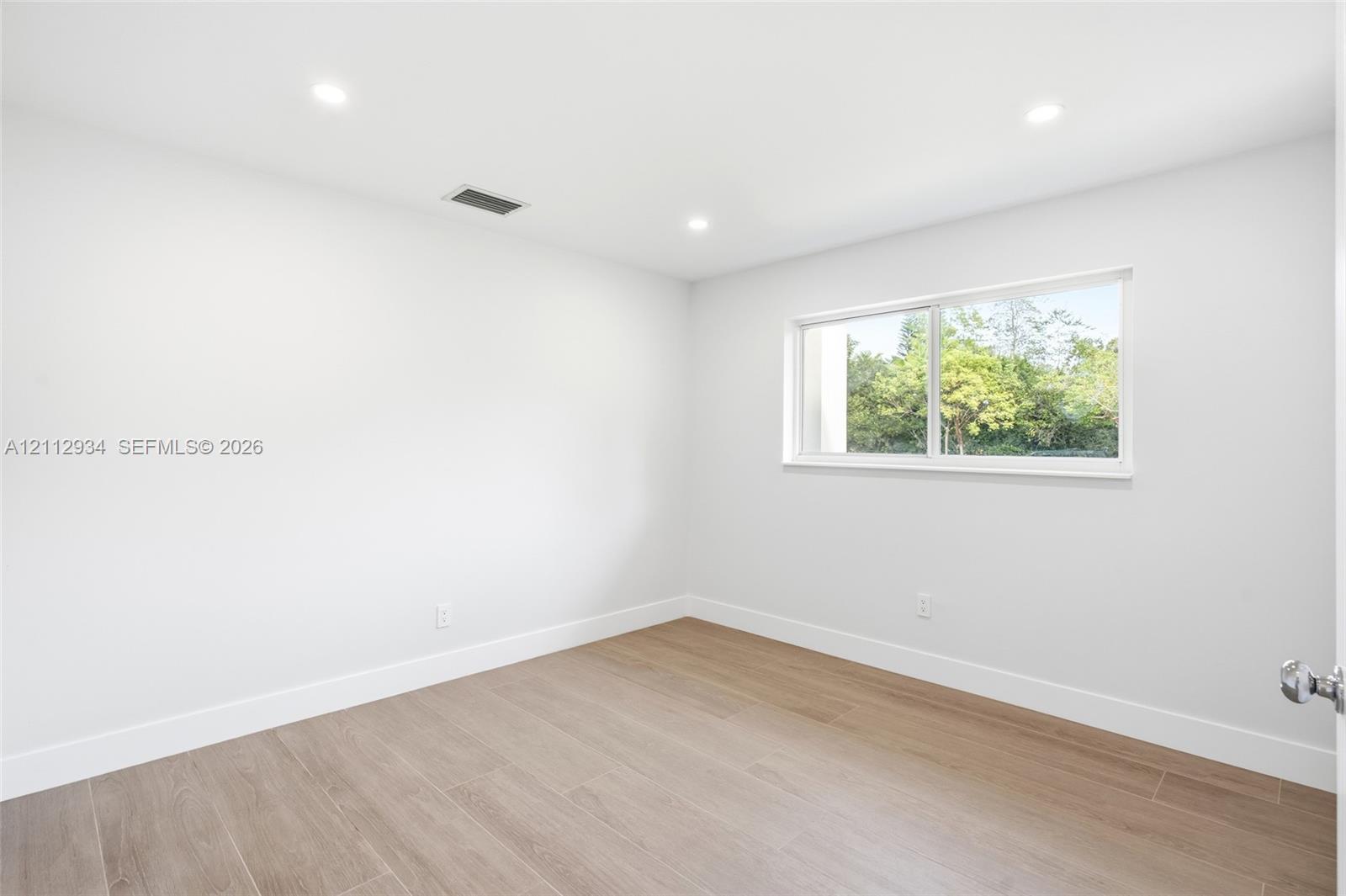 Neutral-toned interior space featuring wood-finish flooring, recessed lighting, and a single-pane slider window