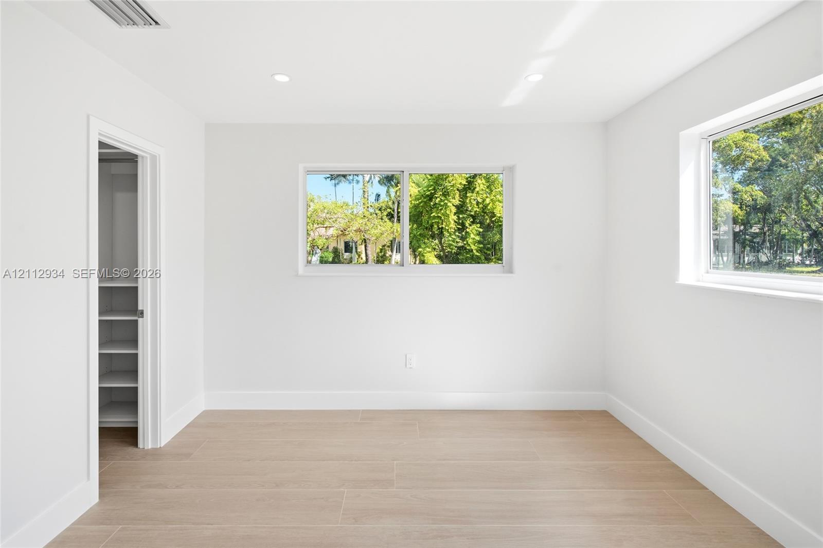 Bright interior featuring wood-finish flooring, recessed lighting, dual sliding windows, and a walk-in closet with built-in shelving