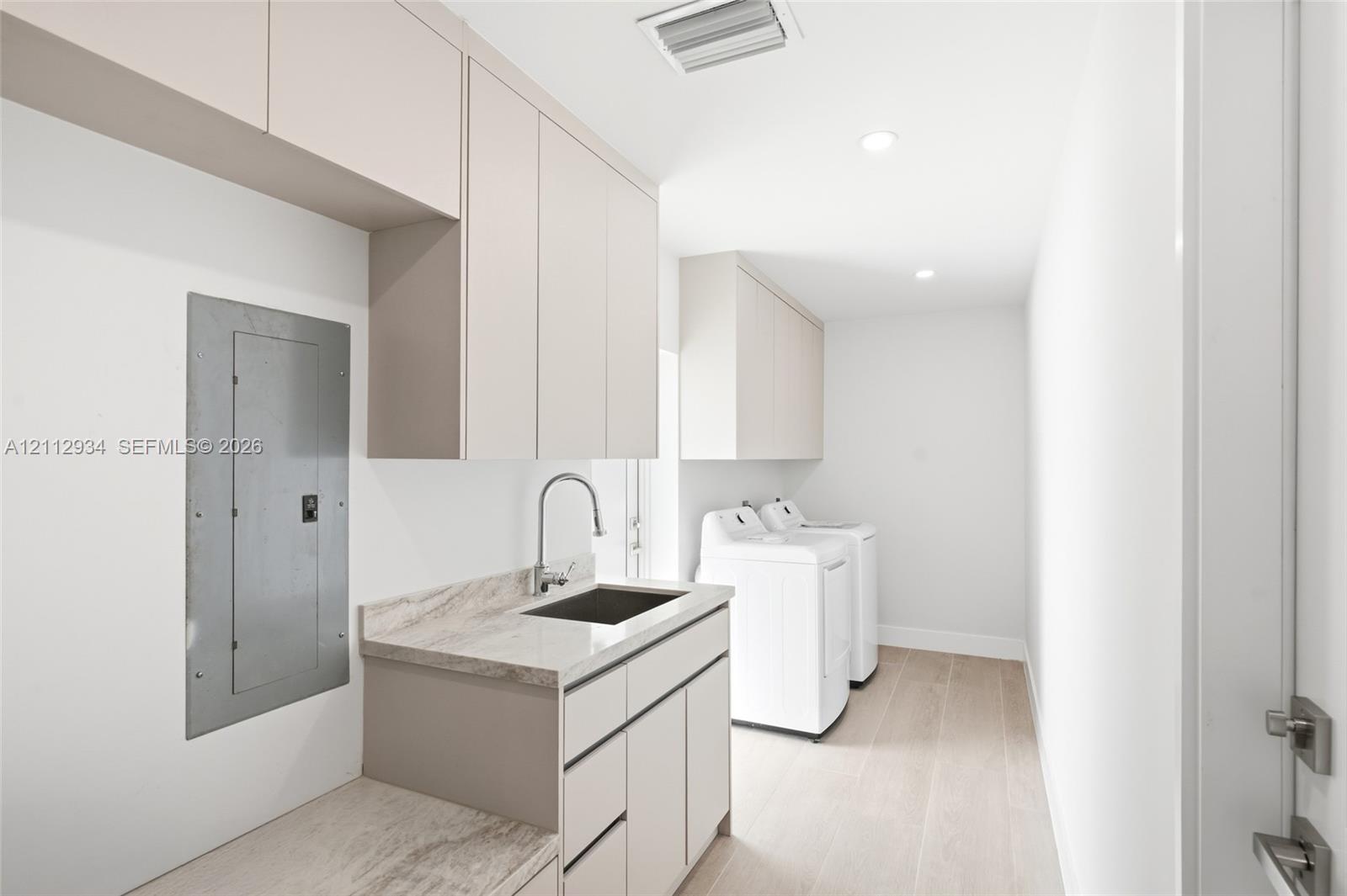 Utility area featuring flat-panel cabinetry, stone-finish countertops, an integrated sink with a gooseneck faucet, and wood-finish flooring