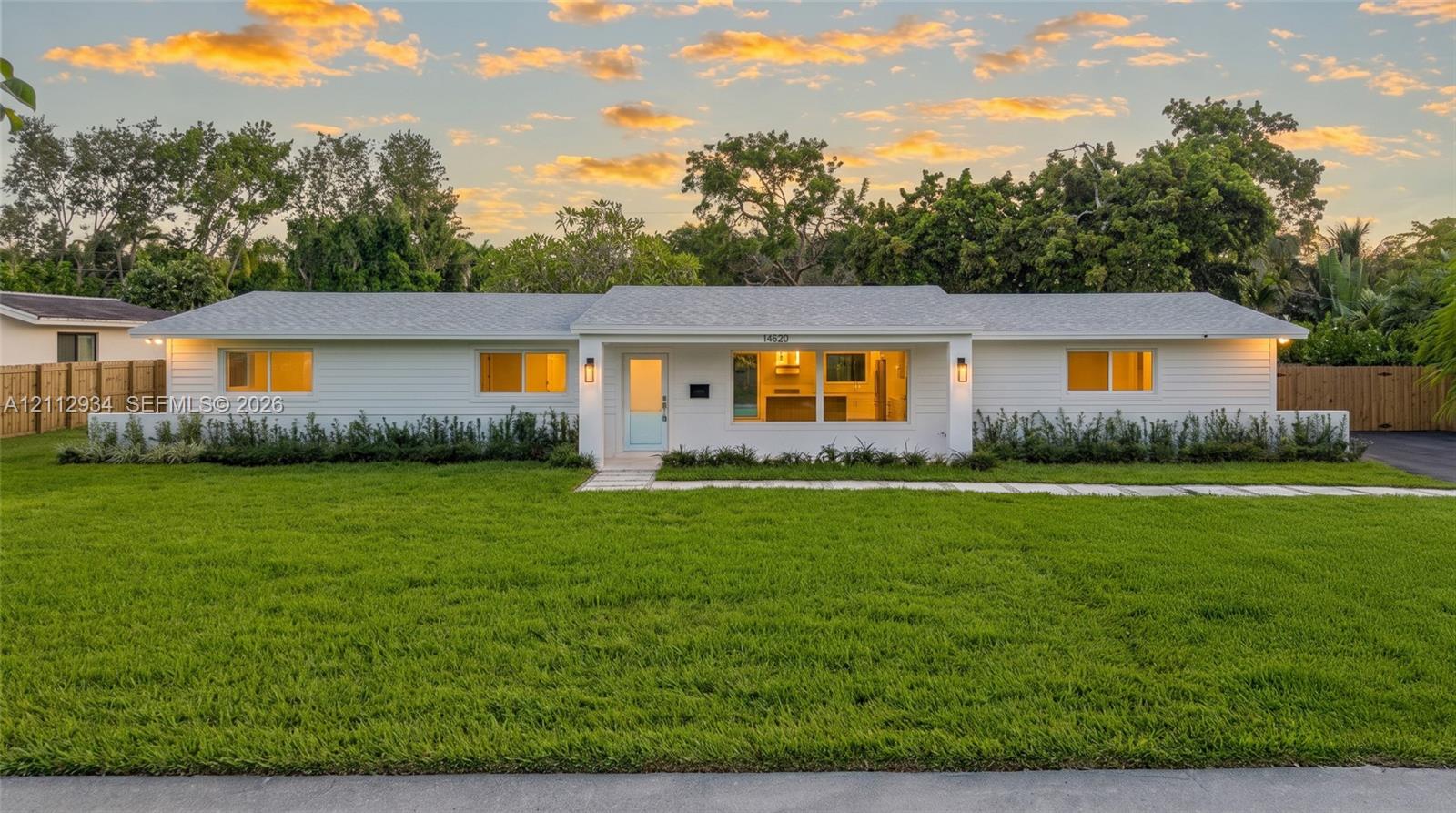 Single-story residence featuring white horizontal siding, a light-toned shingle roof, expansive front lawn, and natural wood-finish privacy fencing