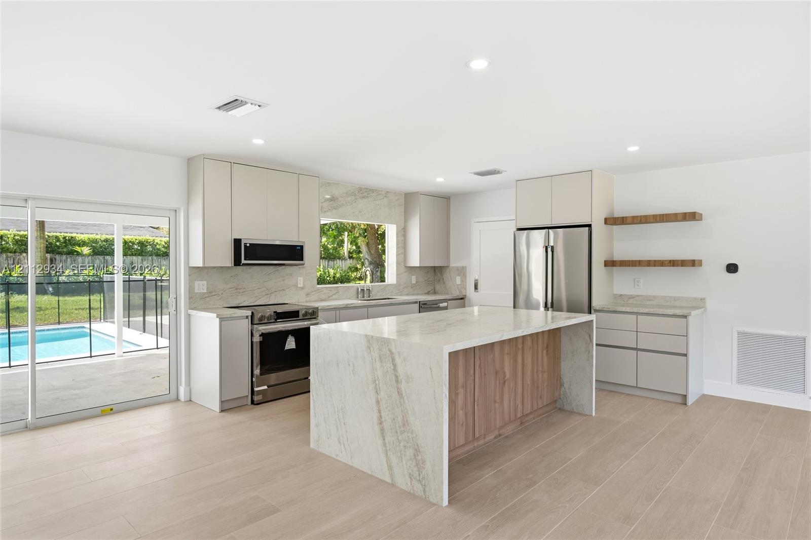 Kitchen featuring a waterfall island with a stone-finish countertop, flat-panel cabinetry, stainless steel appliances, wood-finish flooring, and floating shelving