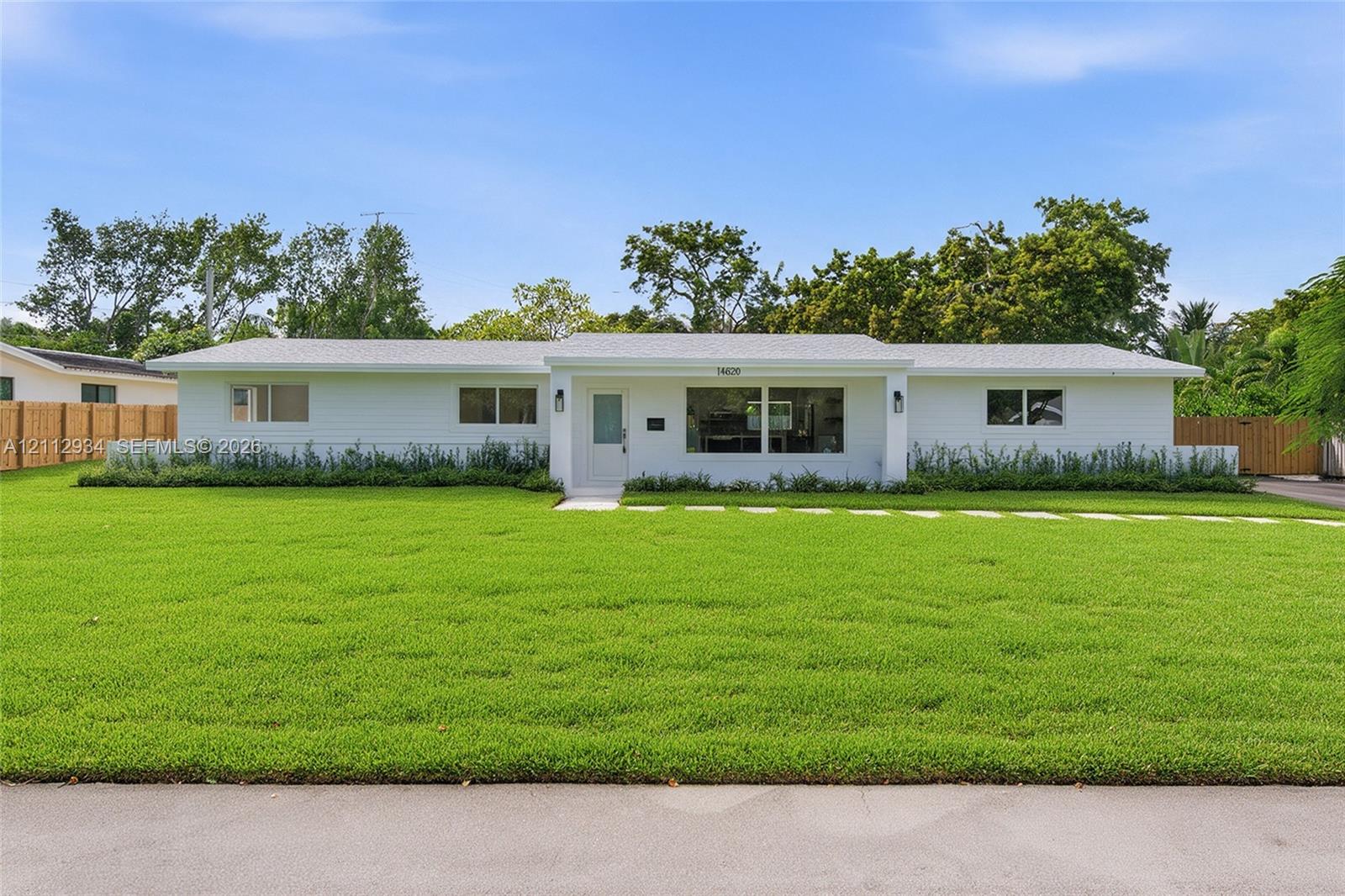 Single-story exterior featuring a white horizontal-siding facade, a neutral shingled roof, a central recessed entrance, and a sprawling front lawn with a stone-paver walkway