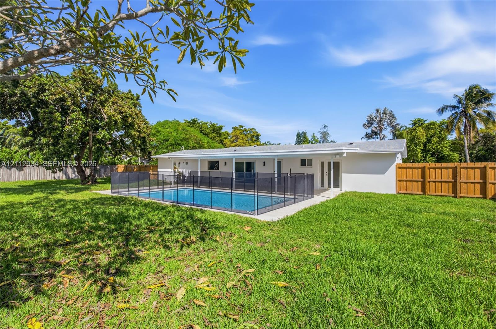 Rear exterior featuring a covered patio, a rectangular swimming pool with a removable safety fence, a concrete pool deck, and a fenced backyard