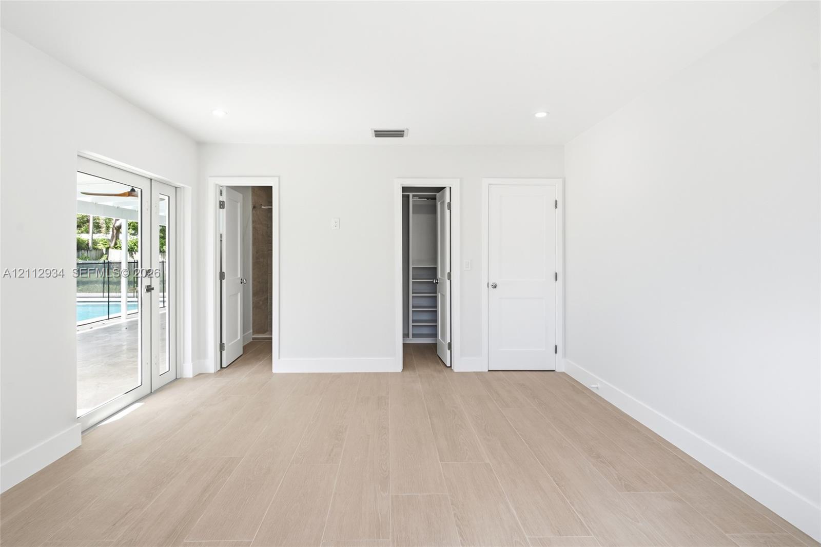 Interior space featuring neutral walls, wood-finish tile flooring, recessed lighting, double glass-panel doors, and built-in closet shelving