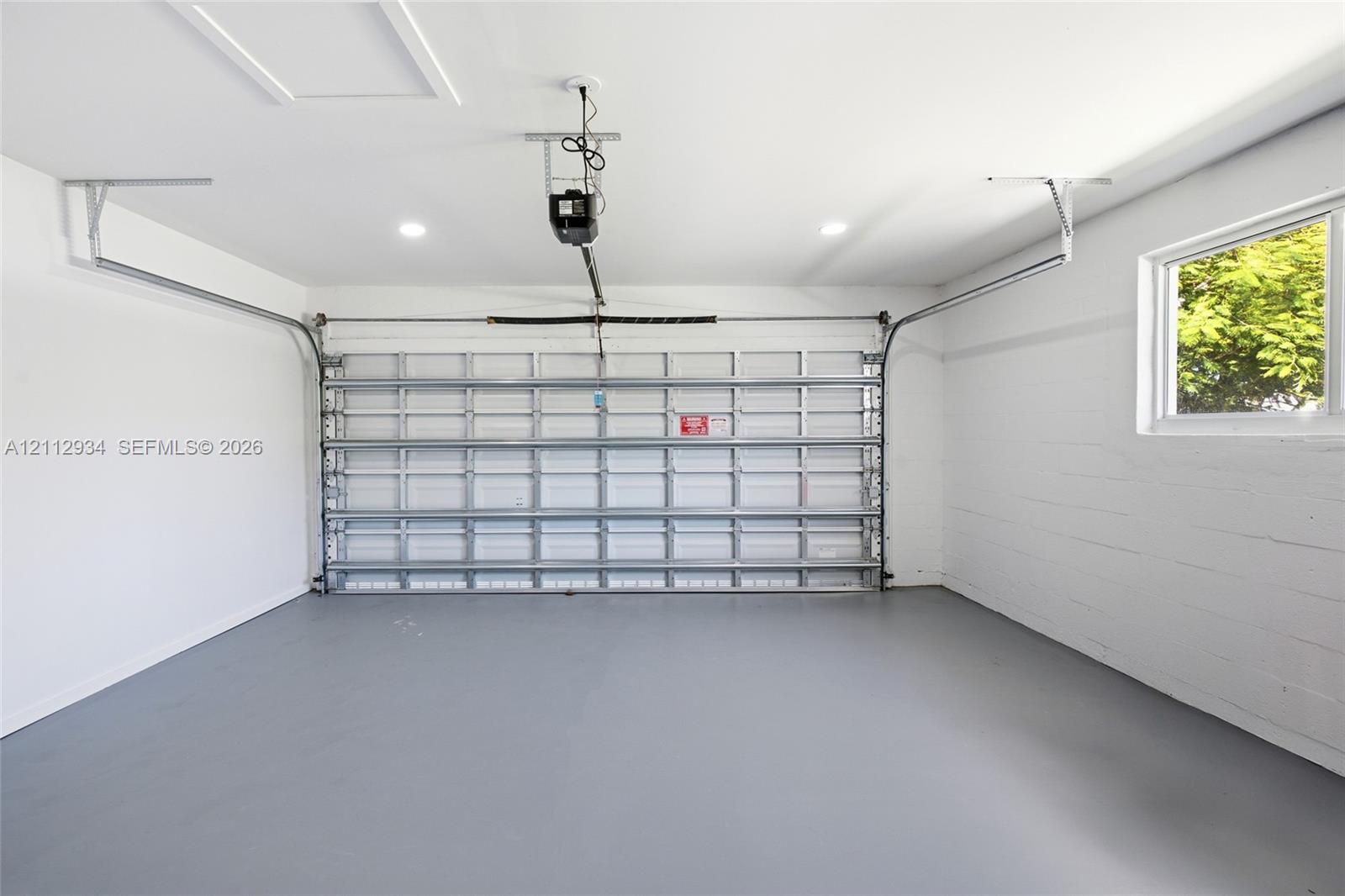 Finished garage featuring white-painted masonry walls, a grey-toned sealed concrete floor, recessed ceiling lighting, and a window providing natural light