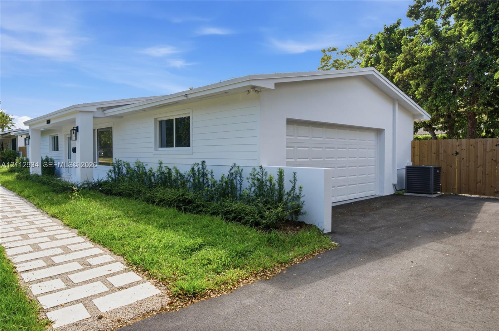 Single-story residence featuring white horizontal lap siding, an attached garage, a paved asphalt driveway, and a stone-paver walkway