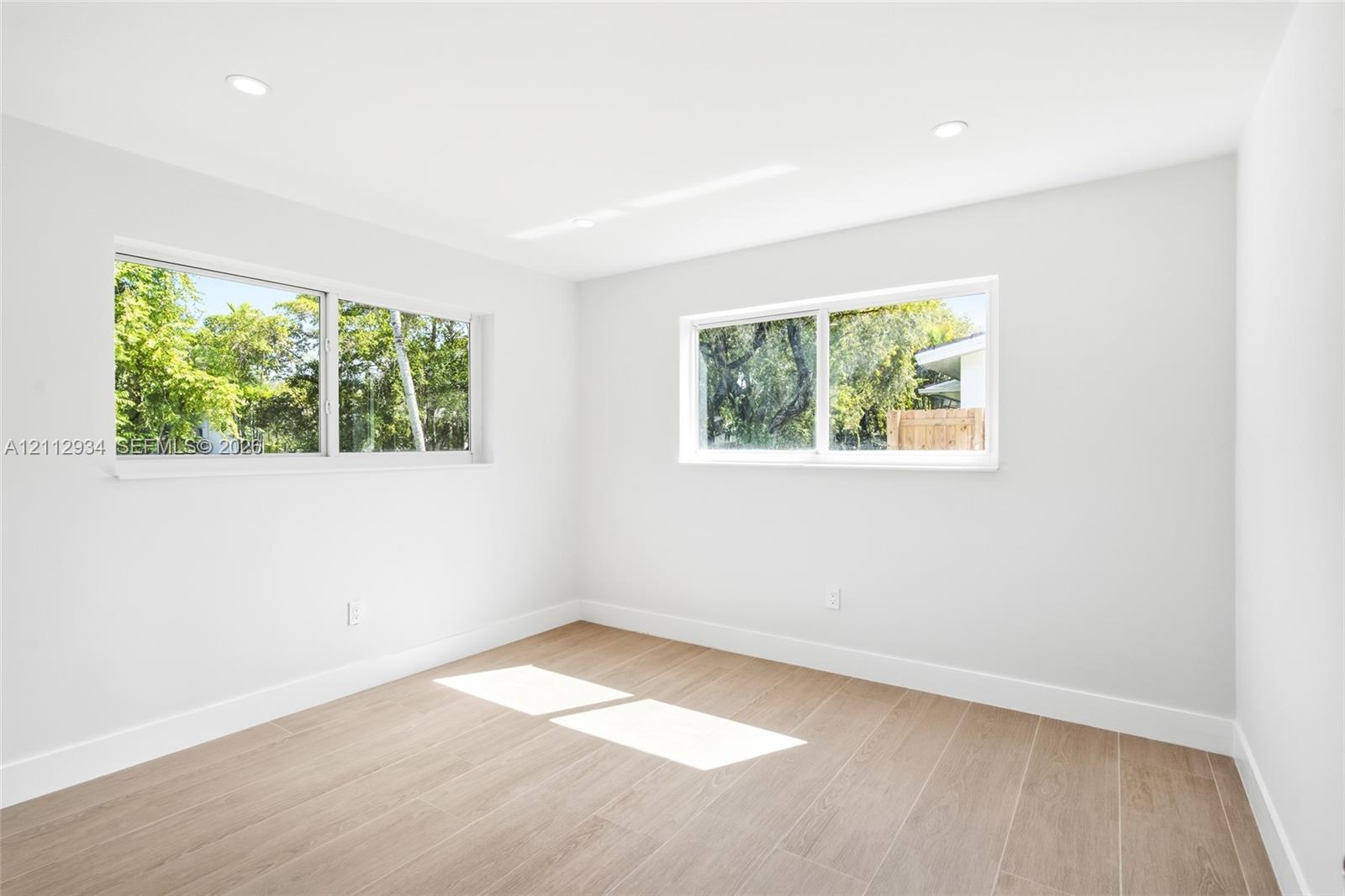 Neutral-toned interior space featuring wood-finish flooring, recessed lighting, and multiple sliding windows