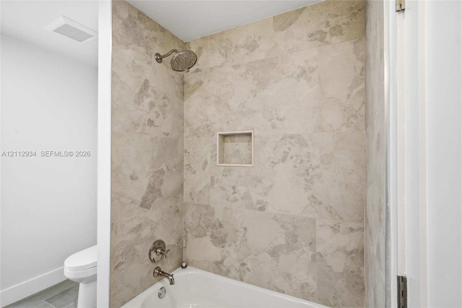 Full-height shower surround with neutral-toned tile, built-in recessed storage niche, and polished metal plumbing fixtures