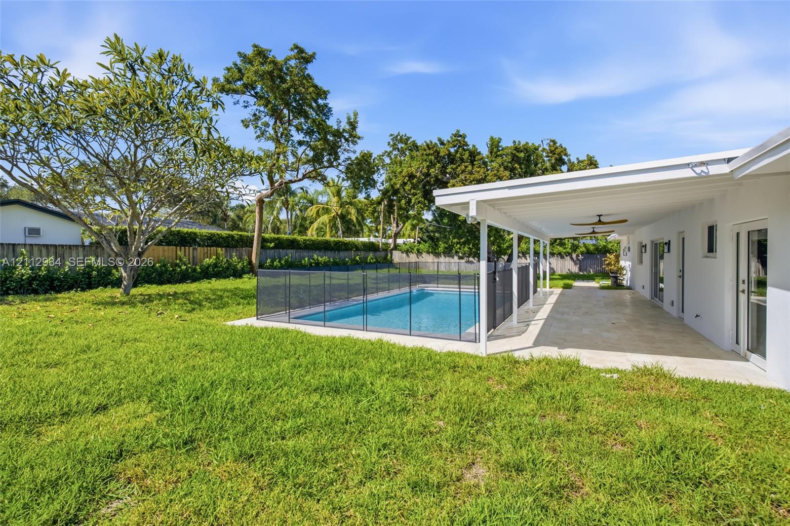 Backyard featuring a swimming pool with a black safety fence, a covered paved patio, and mature landscaping
