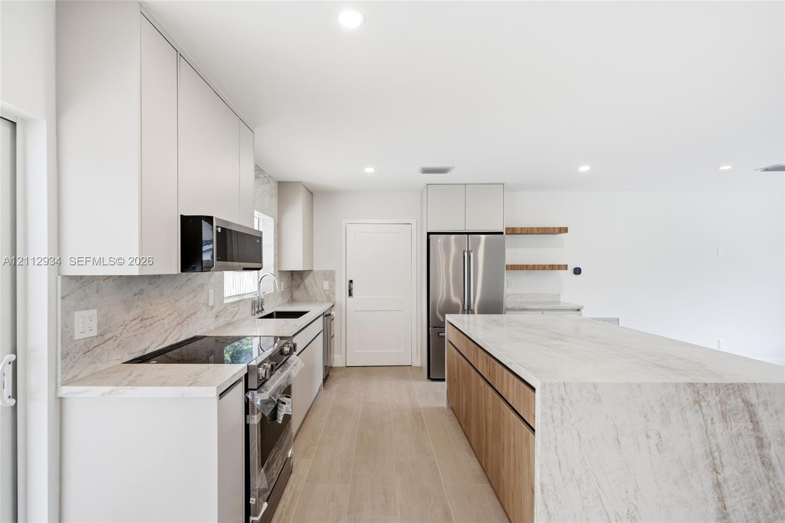 Kitchen featuring waterfall island with stone-finish countertop, flat-panel cabinetry, stainless steel appliances, and wood-finish flooring