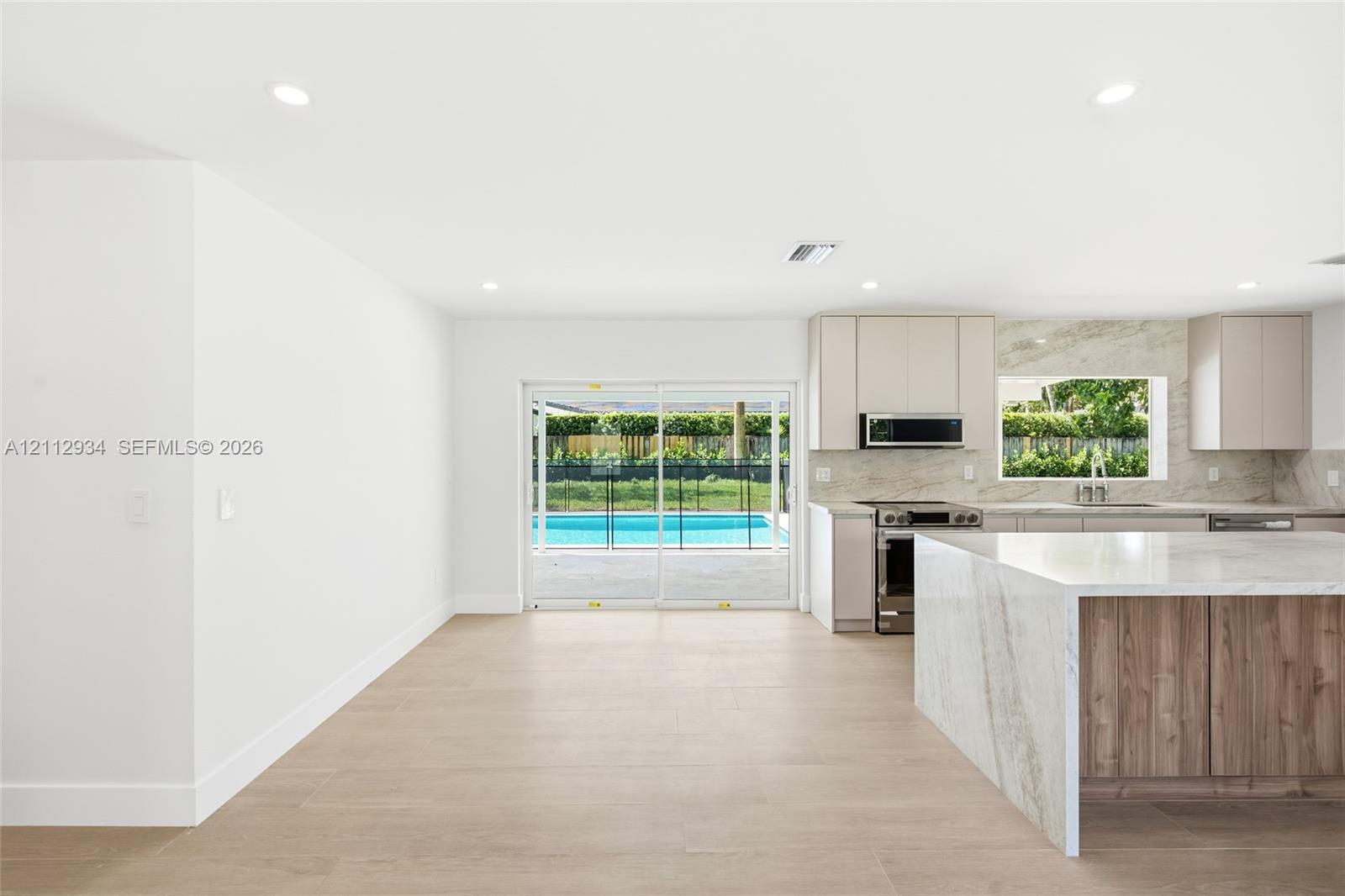 Kitchen featuring a waterfall island with stone-finish countertops, wood-finish cabinetry, recessed lighting, and large-format tile flooring