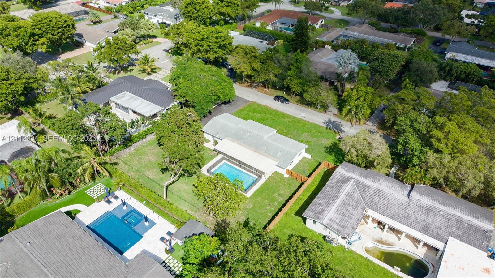 Aerial perspective featuring a single-story residence with a pitched roof, private in-ground swimming pool, expansive lawn area, and perimeter wood fencing