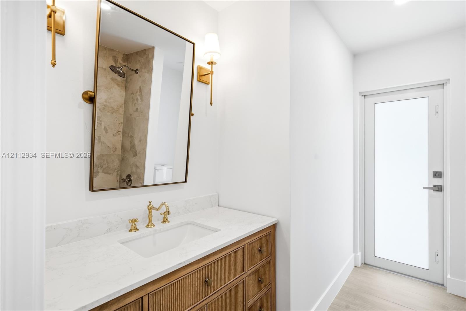 Custom wood-finish vanity with a stone countertop, undermount sink, brass-tone hardware, and wall-mounted sconces
