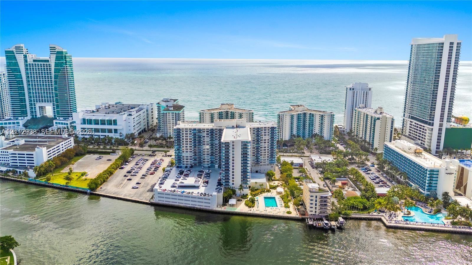 Aerial perspective of coastal high-rise development featuring water frontage, multiple swimming pools, and integrated parking structures