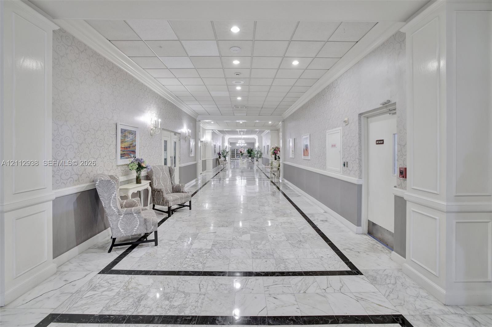 Hallway featuring polished stone flooring with decorative inlay, wall molding, neutral wallpaper, and recessed ceiling lighting