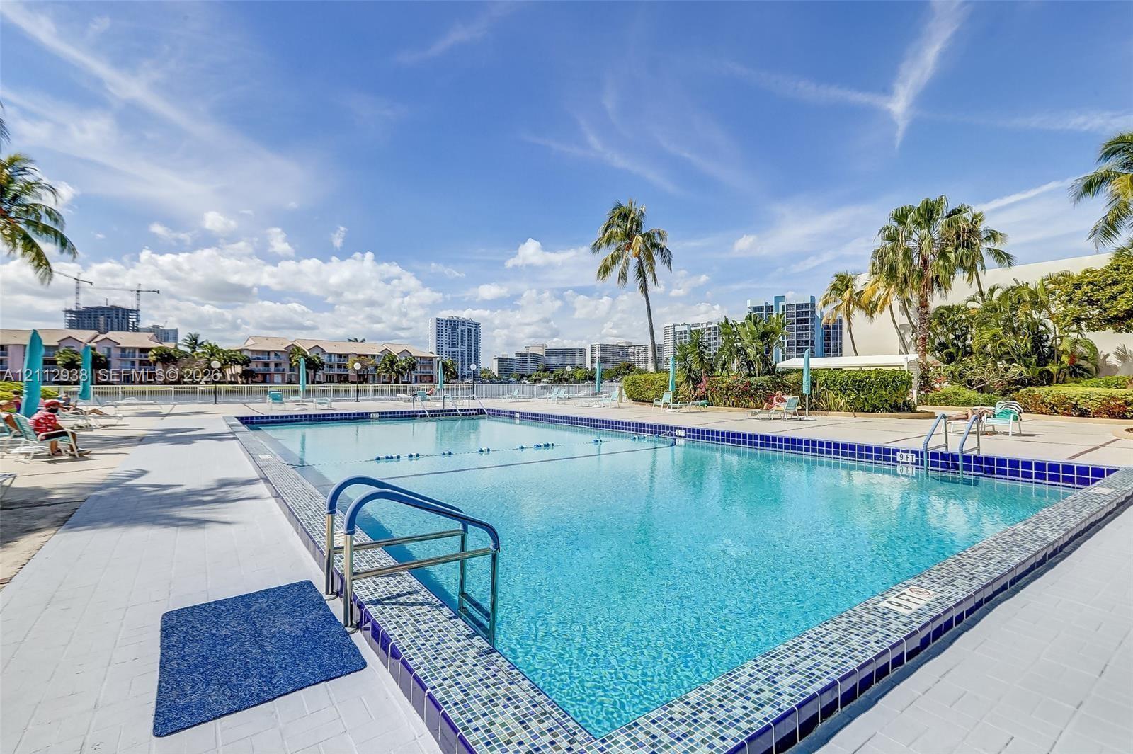 Swimming pool featuring a decorative glass tile border, metal handrails, and a concrete deck surround