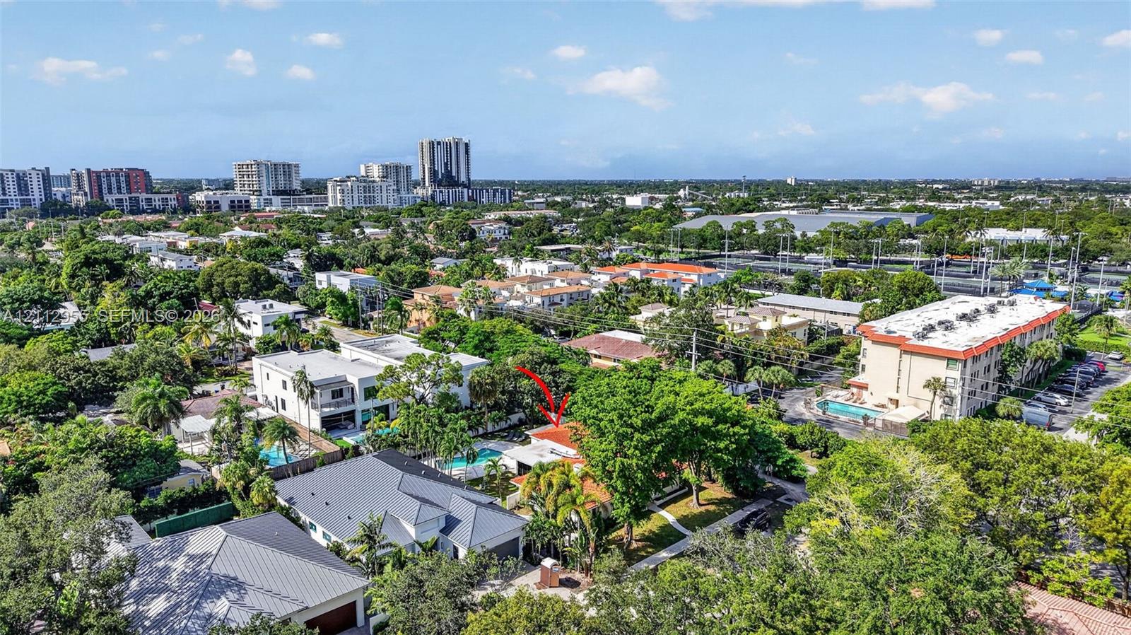 Aerial perspective of a property featuring a swimming pool, mature canopy trees, and a low-pitch roofline within a dense residential setting