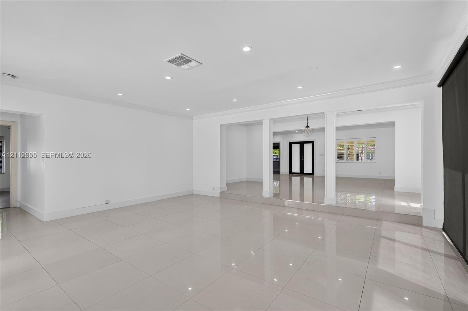 Open-concept interior featuring large-format tile flooring, recessed lighting, crown molding, and structural columns