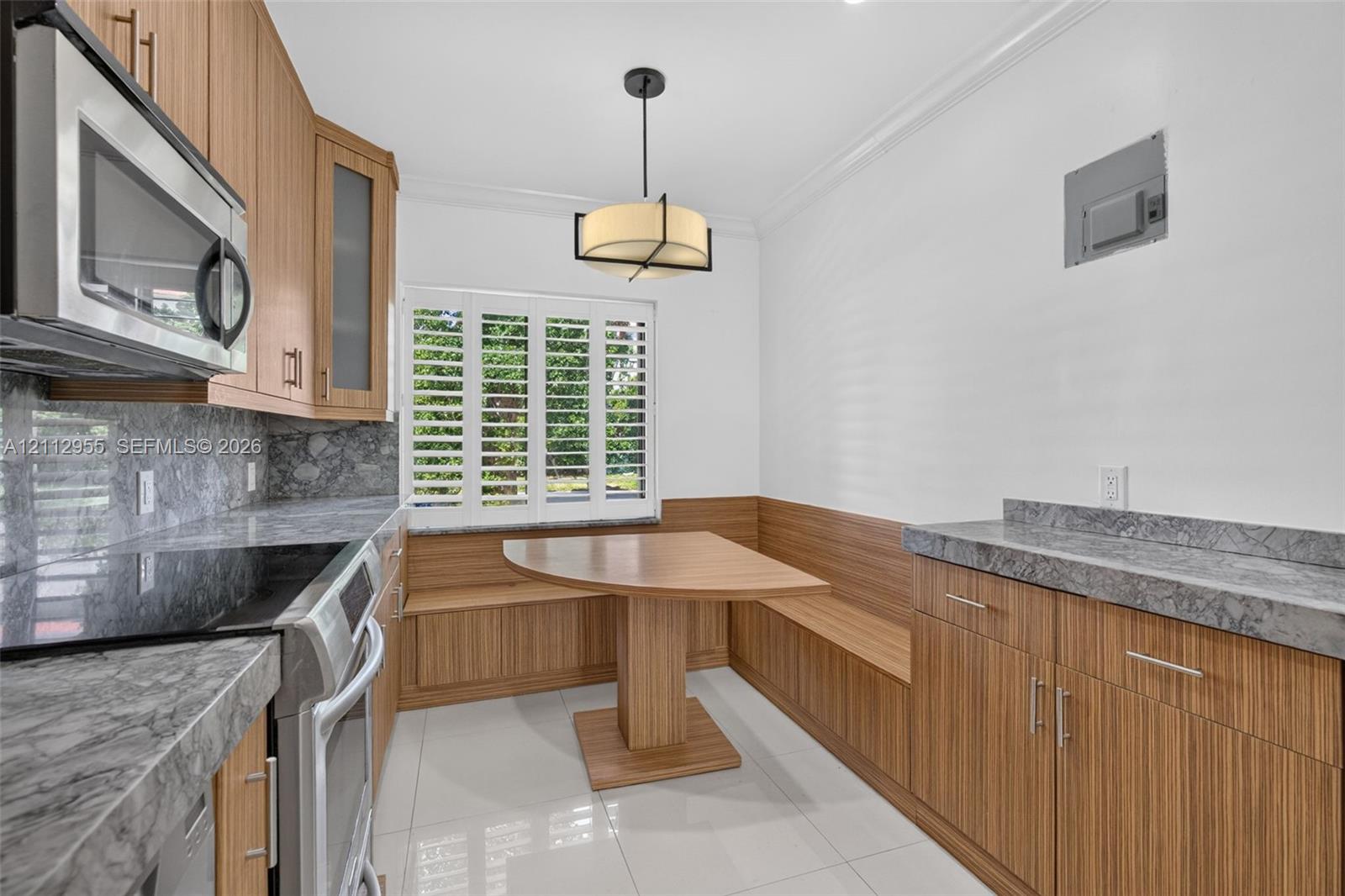 Kitchen featuring wood-finish cabinetry, stone-surface countertops, built-in breakfast nook with integrated bench seating, polished tile flooring, and shutter window treatments