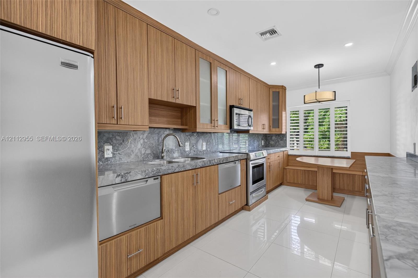 Kitchen featuring wood-grain cabinetry, stone countertops with matching backsplash, stainless steel appliances, polished tile flooring, and a built-in bench seating nook