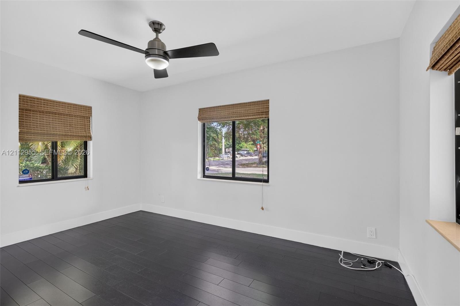 Dark-toned wood-finish flooring, matte black ceiling fan with integrated lighting, and woven bamboo window shades