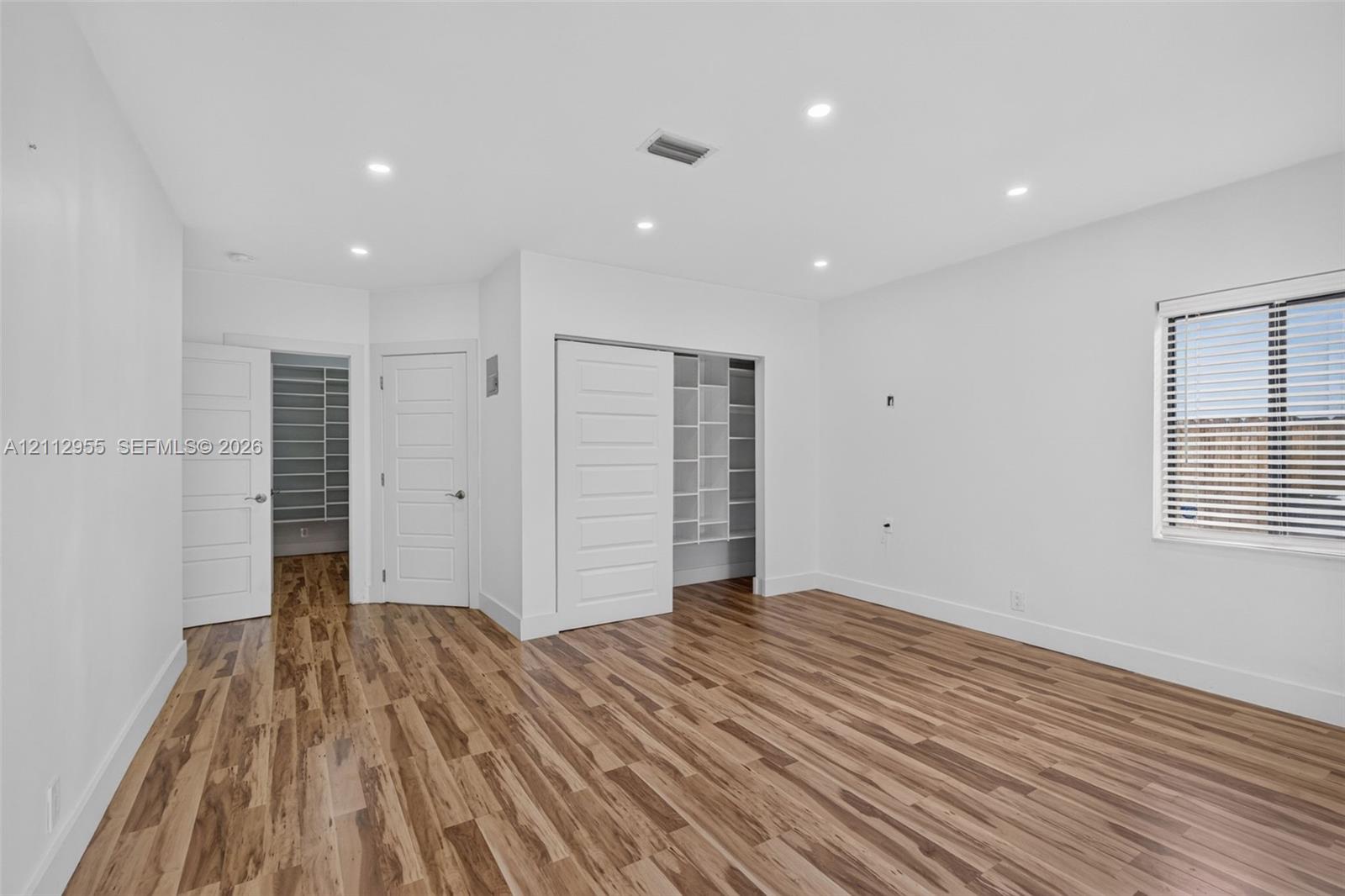Room featuring wood-finish flooring, recessed lighting, white horizontal-panel doors, and built-in shelving within the closet space