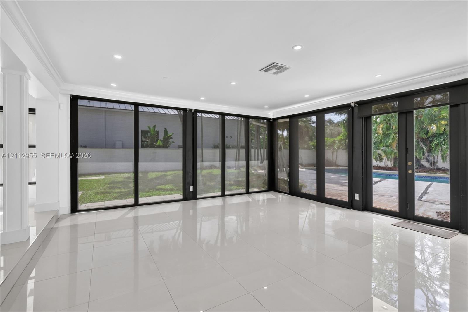 Polished porcelain tile flooring, recessed LED lighting, and expansive floor-to-ceiling black-framed glass wall panels opening to a rear exterior patio and pool area