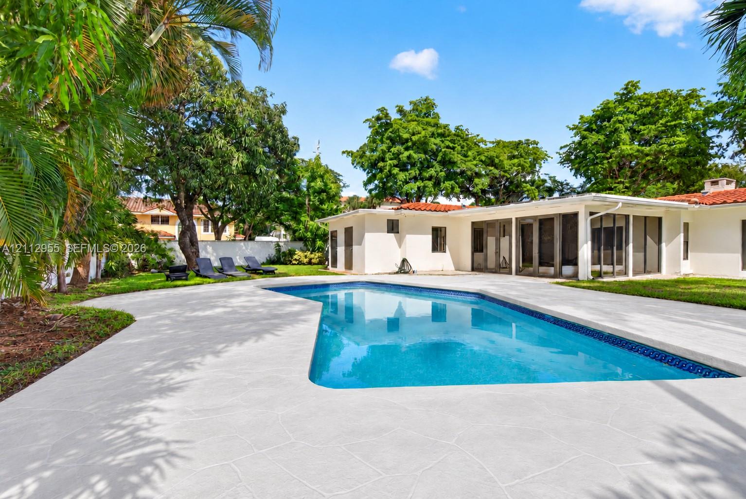 Backyard featuring an in-ground swimming pool, expansive concrete patio, screened-in lanai, and mature landscaping