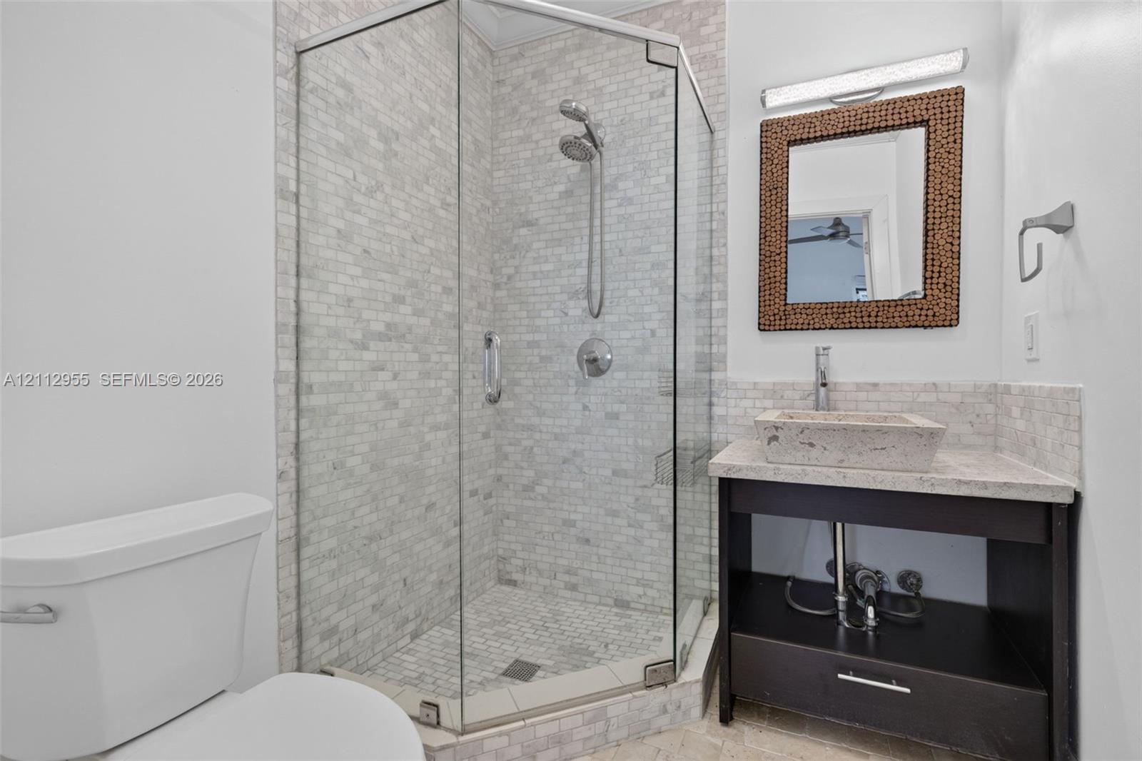 Corner shower enclosure with glass panels, stone-tiled walls, and a handheld showerhead