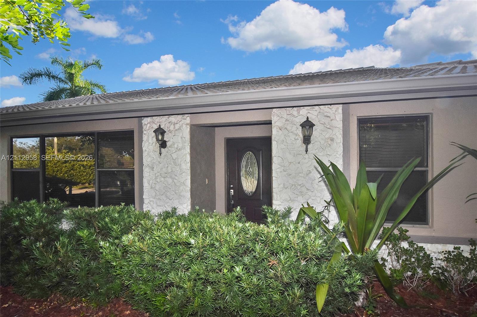 Single-story exterior featuring a textured stone veneer facade, dark-frame windows, a central front entry with an oval glass insert, and exterior wall-mounted carriage lights