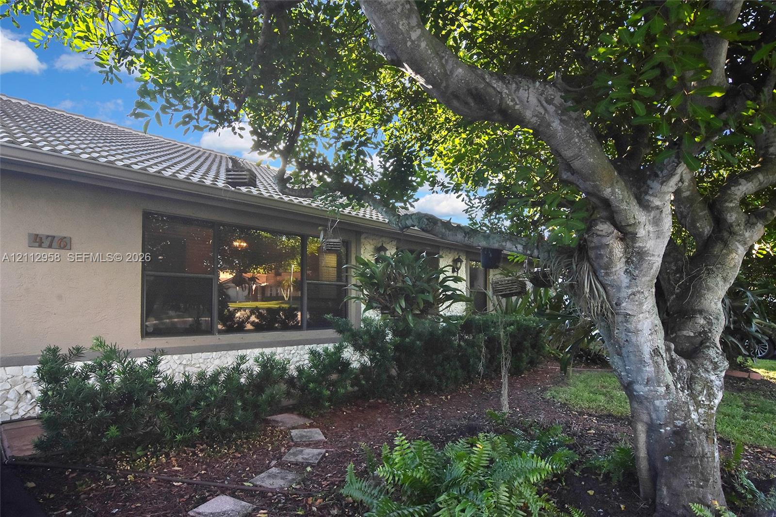 Exterior facade featuring stucco siding, stone veneer base, tiled roof, large picture window, and mature landscaping