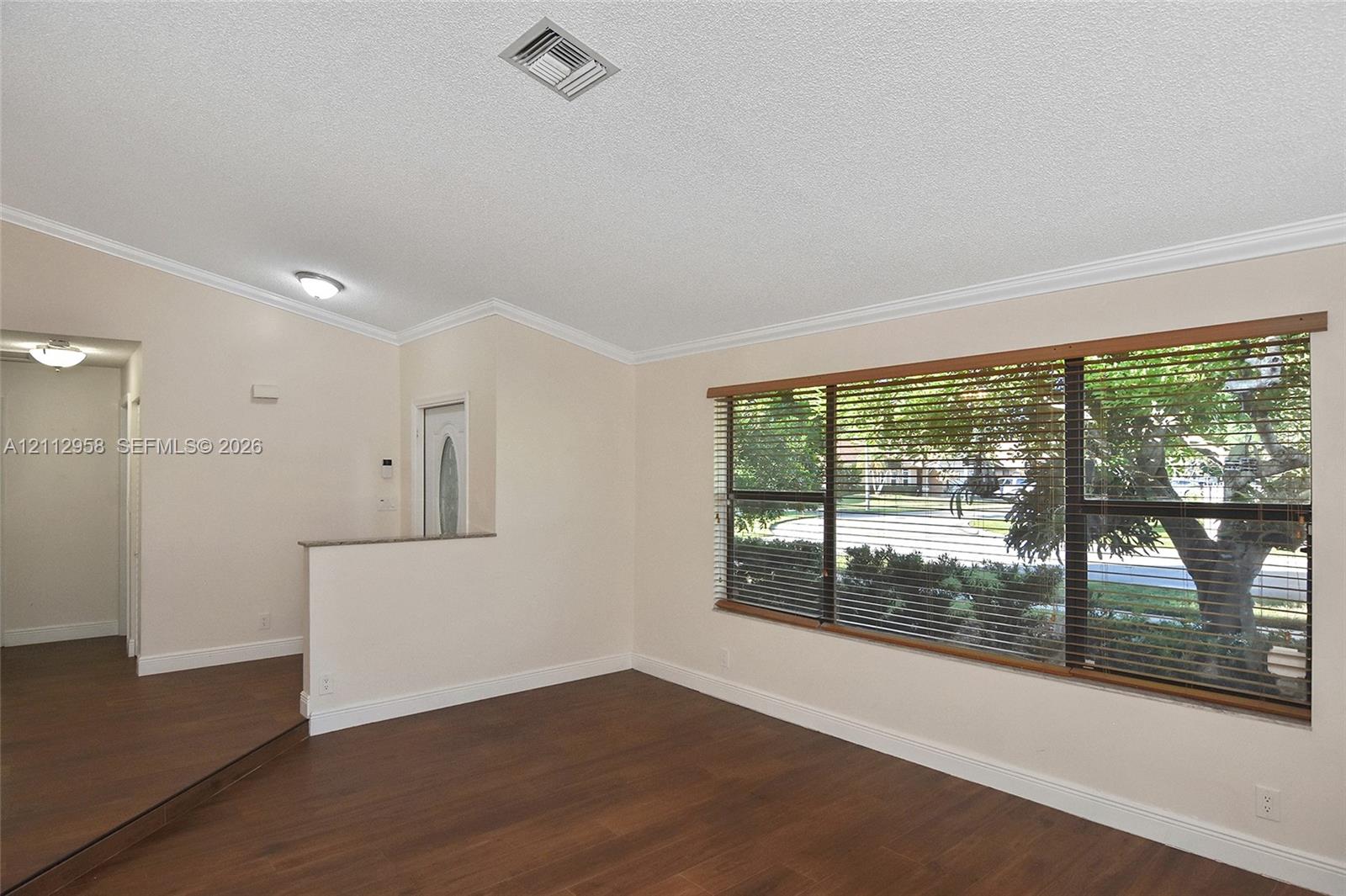 Interior space featuring wood-finish flooring, a large picture window with wood-trim, crown molding, and a partial partition wall