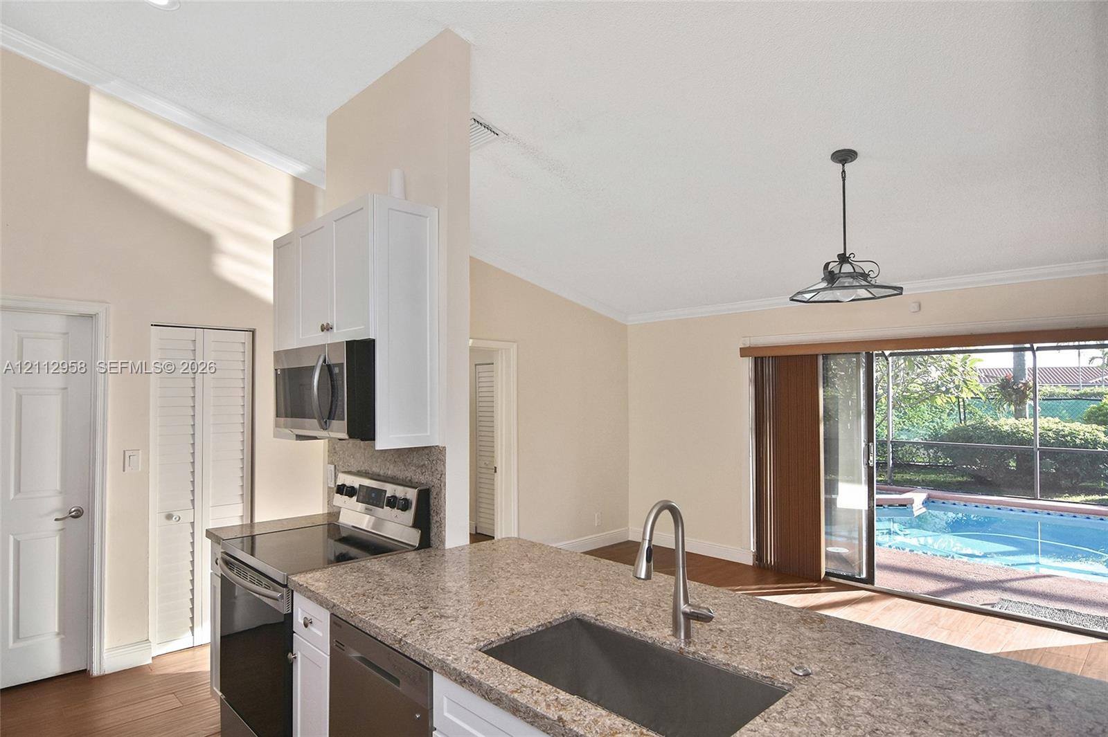 Kitchen featuring stone-finish countertops, stainless steel appliances, vaulted ceilings, and a sliding glass door providing access to the pool area