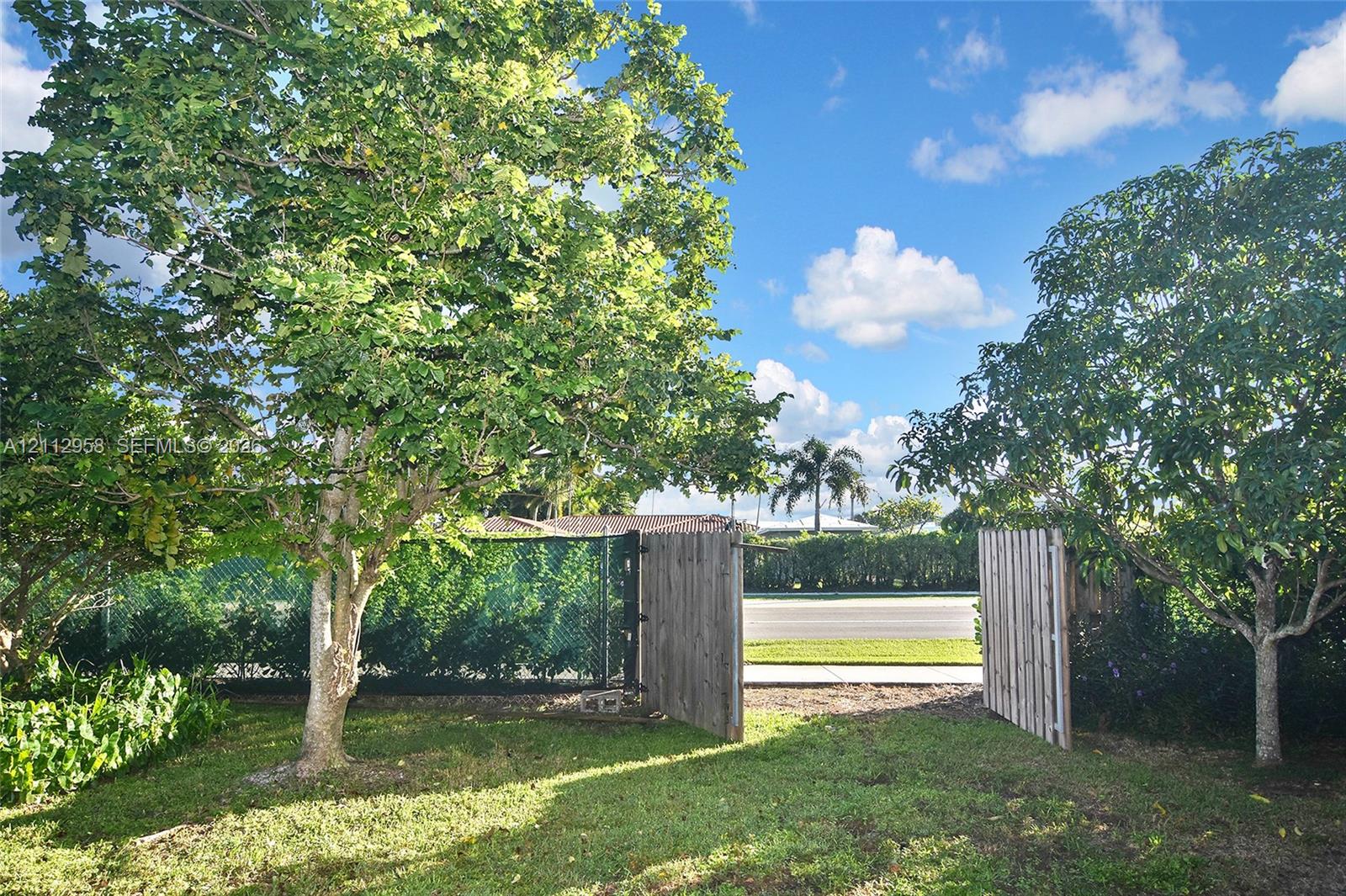 Fenced grounds featuring mature trees, a manicured lawn, and a wooden privacy gate