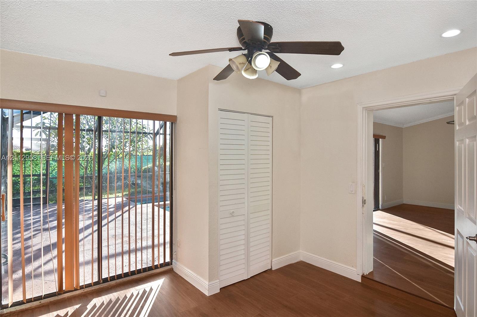Wood-finish flooring, sliding glass door with vertical blinds, white louvered-door closet, ceiling fan with integrated lighting, and recessed ceiling lights