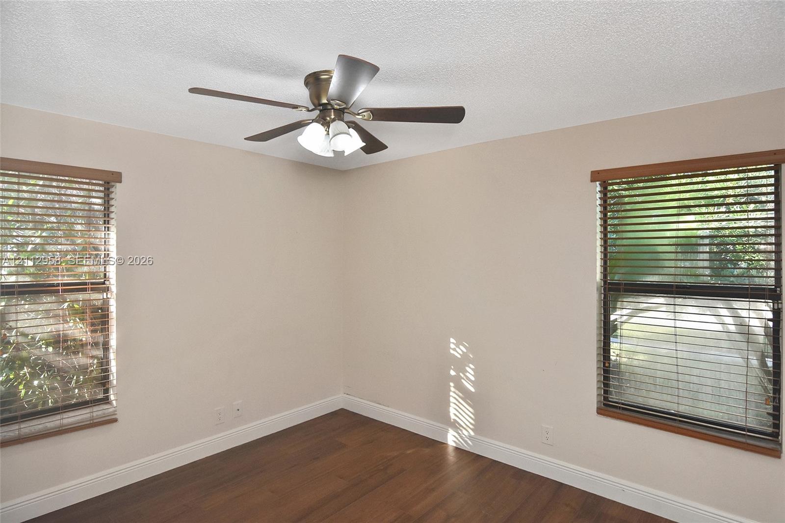 Interior space featuring wood-finish flooring, two dual-pane windows with horizontal blinds, and a multi-blade ceiling fan with an integrated light fixture