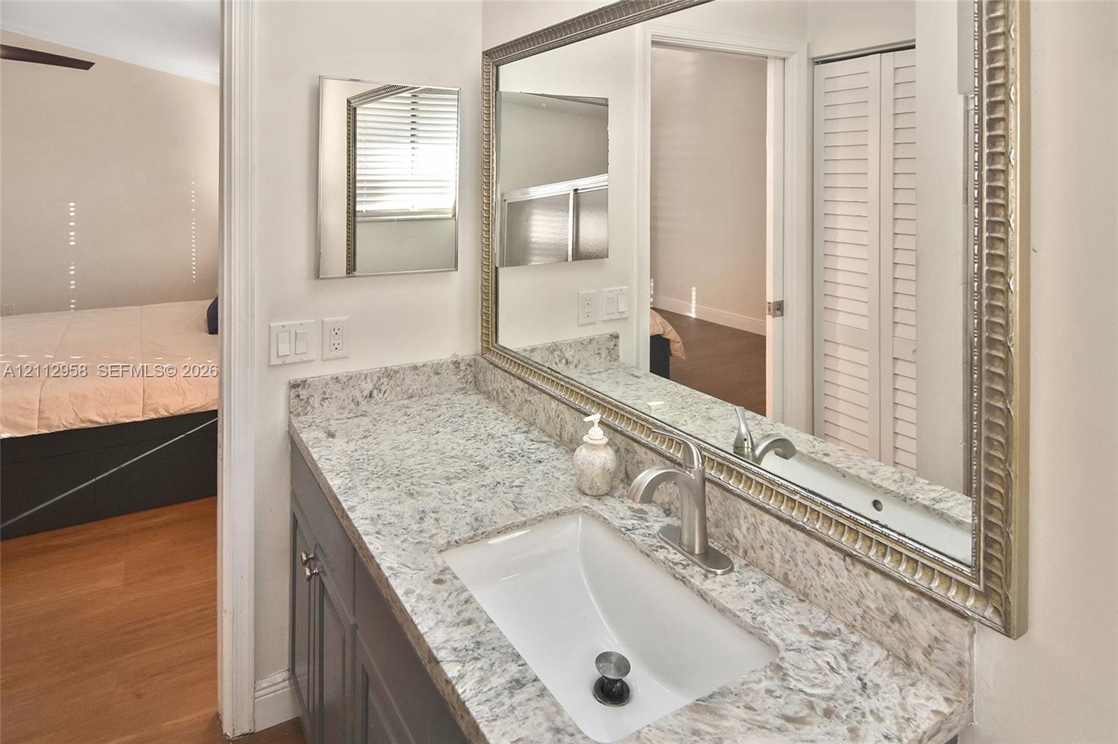 Bathroom vanity featuring a stone countertop, an integrated rectangular sink, a brushed nickel faucet, a large wall-mounted mirror with a metallic frame, and cabinetry with louvered closet doors