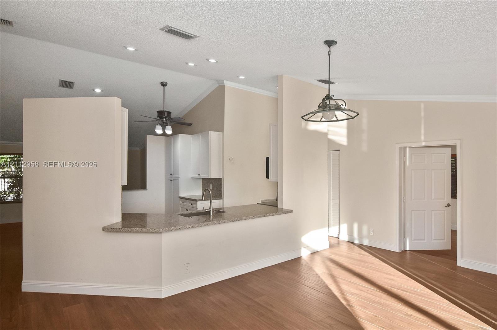 Open-concept kitchen featuring a breakfast bar with stone-finish countertop, stainless steel sink, white cabinetry, wood-finish flooring, and vaulted ceilings with recessed lighting
