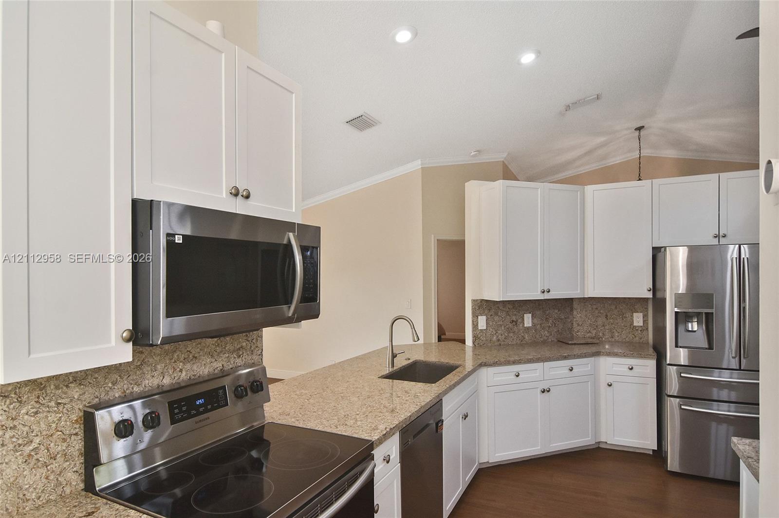Kitchen featuring white cabinetry, stone countertops, stainless steel appliances, and wood-finish flooring under recessed lighting