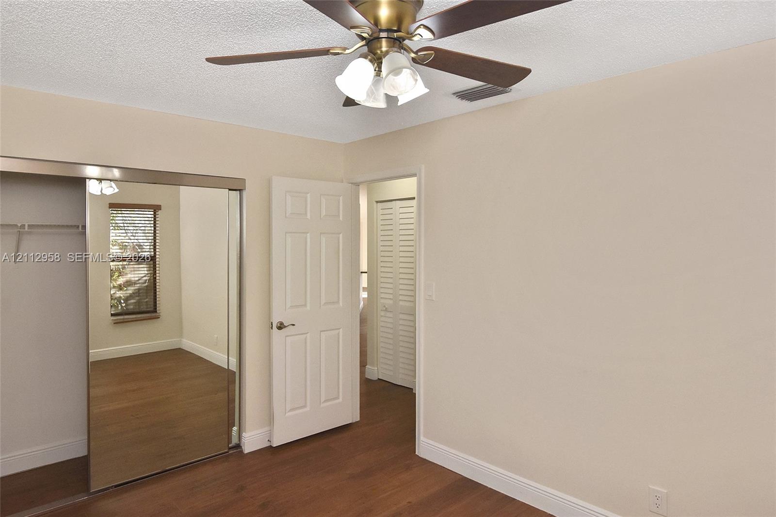 Wood-finish flooring, ceiling fan with three-light fixture, mirror-paneled sliding closet doors, and six-panel interior door