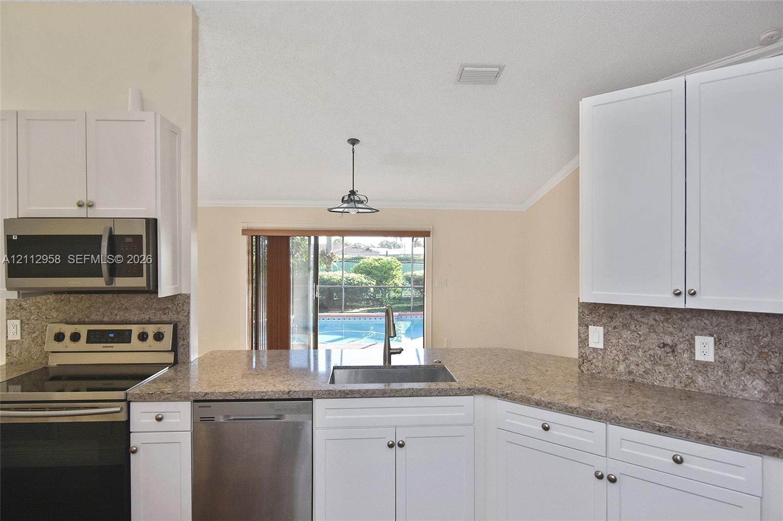 Kitchen featuring white shaker-style cabinetry, stone-patterned countertops, stainless steel appliances, a double-basin sink, and a vaulted ceiling