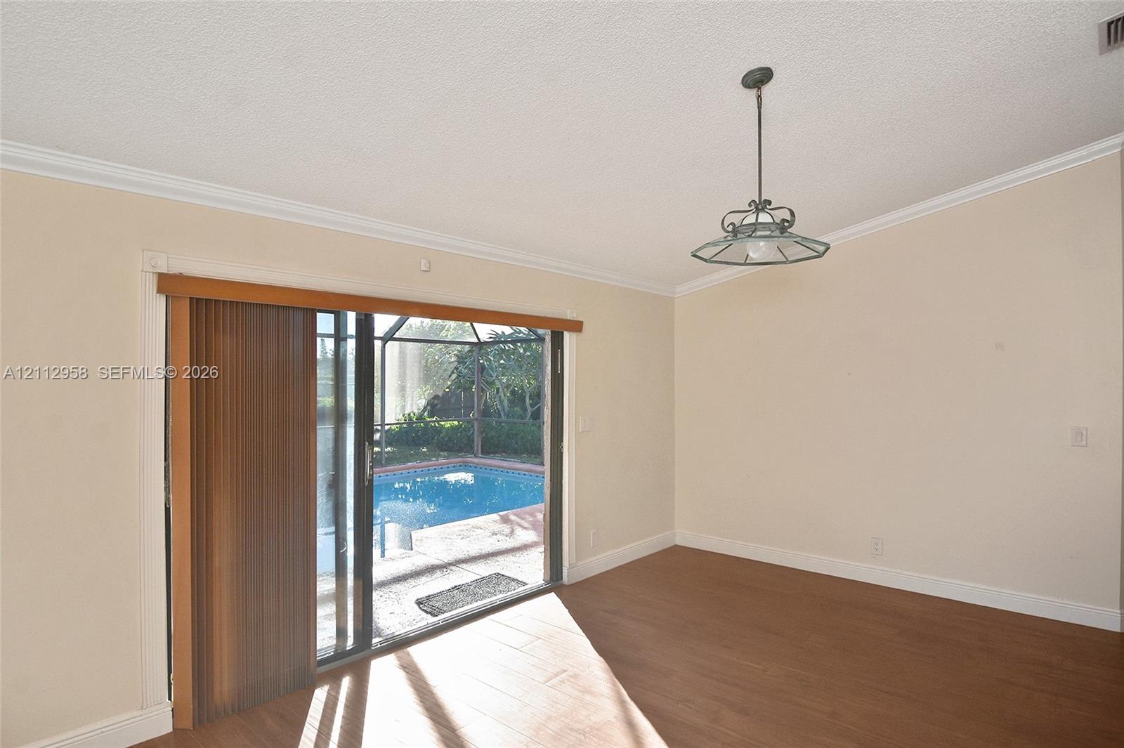 Interior space featuring wood-finish flooring, a tiered metal pendant light fixture, and sliding glass doors opening to an enclosed pool area