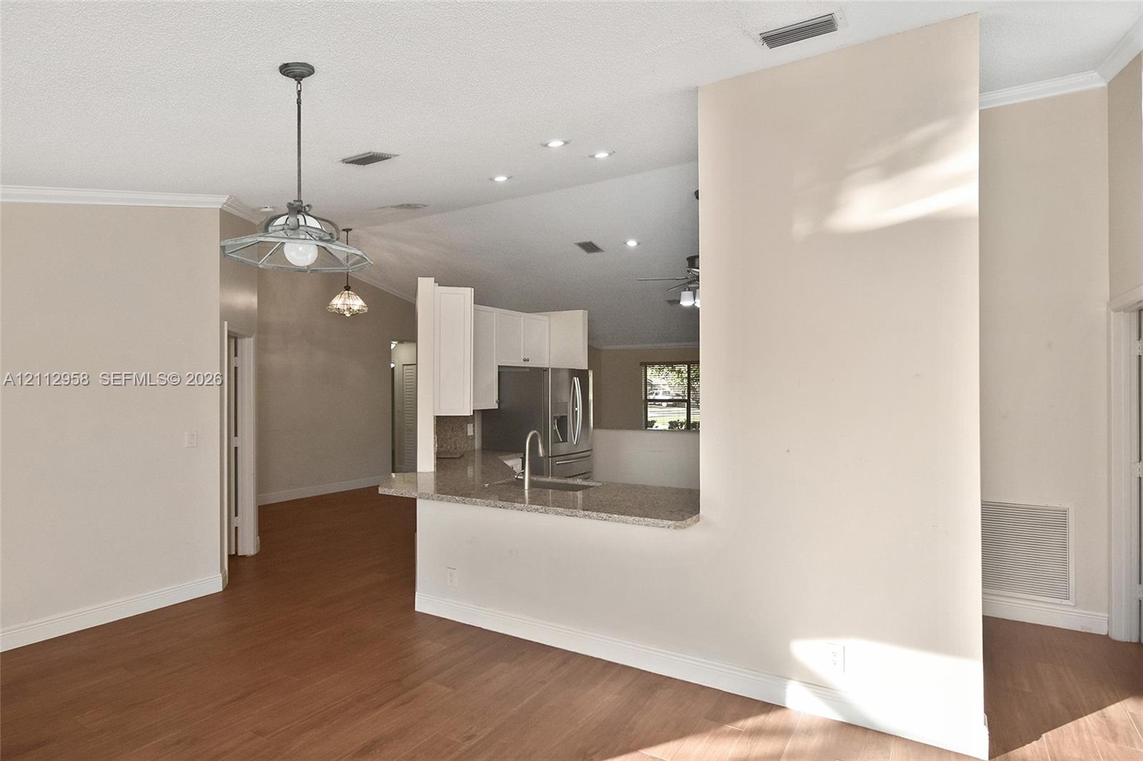 Kitchen featuring stone-finish countertops, stainless steel refrigerator, white cabinetry, wood-finish flooring, and pendant lighting