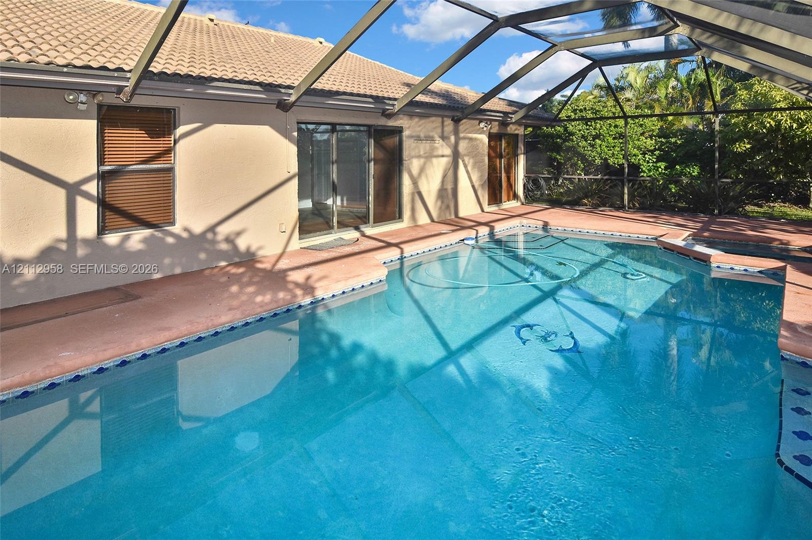 In-ground swimming pool featuring a tiled waterline, enclosed by a screened lanai with a concrete deck, concrete tile roofing, and sliding glass exterior doors