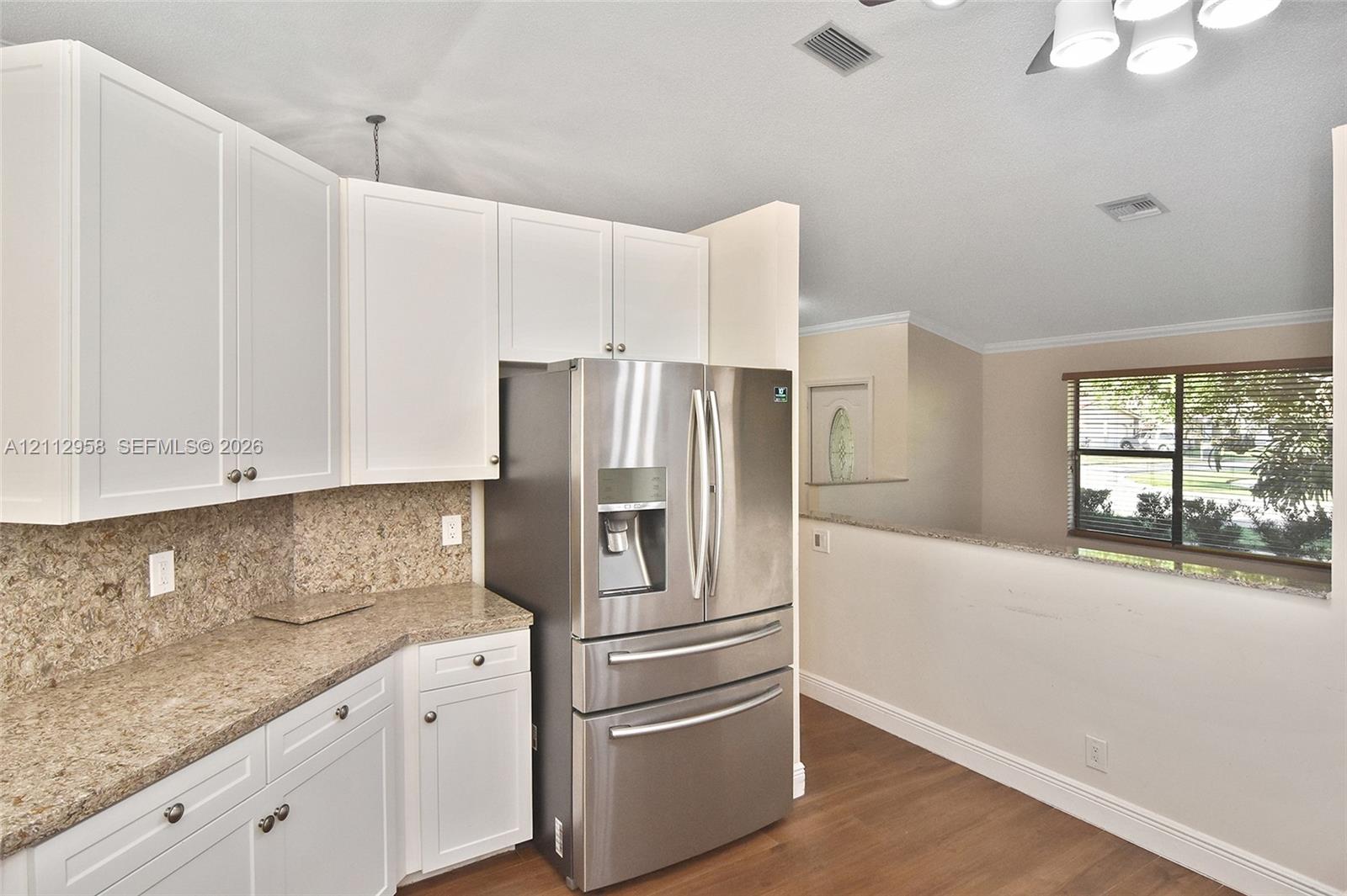 Kitchen featuring white shaker-style cabinetry, speckled stone-finish countertops, stainless steel French-door refrigerator, and wood-finish flooring