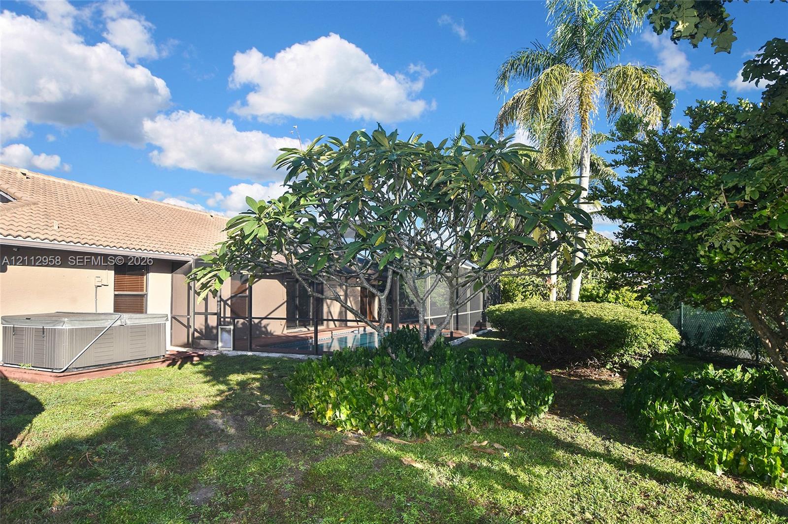 Backyard featuring a screen-enclosed pool area, an attached exterior hot tub, mature landscaping, and palm trees