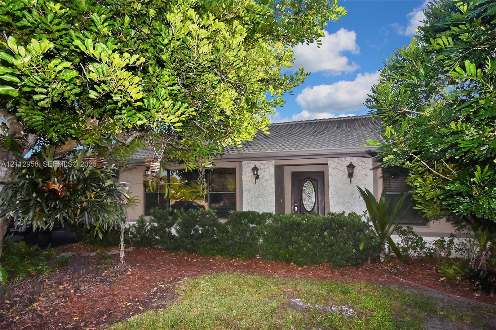 Exterior facade featuring a textured stone finish, tiled roof, decorative front door with an oval glass insert, and dual wall-mounted coach lights