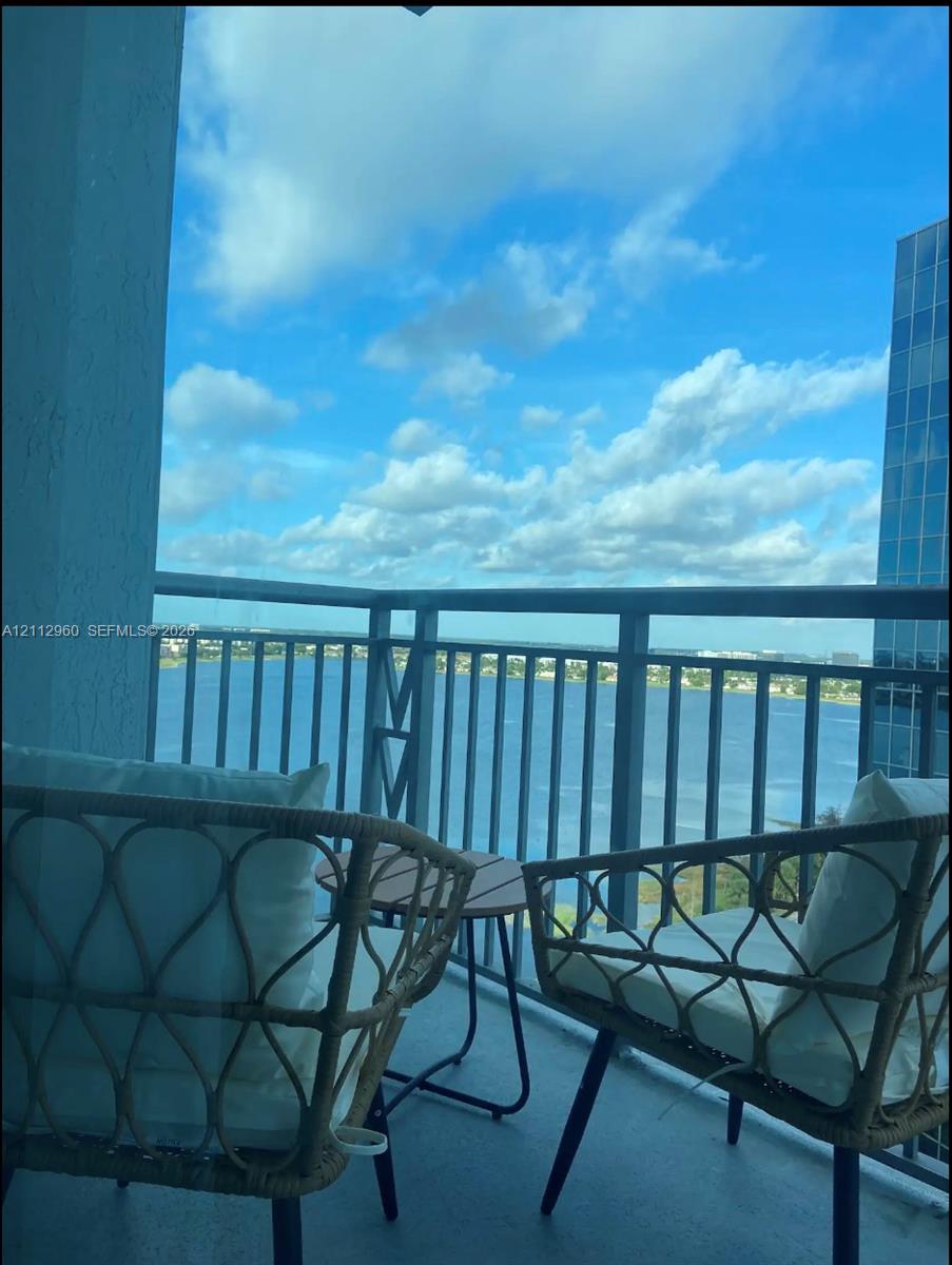 Covered balcony featuring metal railings and concrete flooring with water and skyline scenery