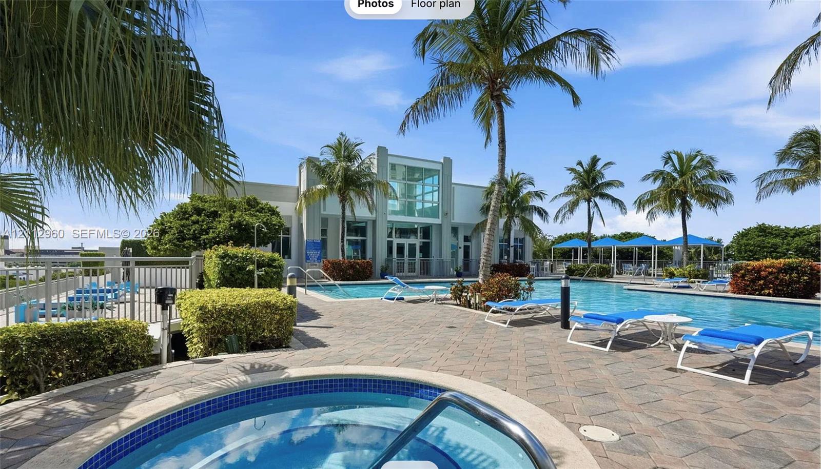 Swimming pool area featuring a stone paver deck, built-in spa with blue tile trim, palm trees, and shade structures