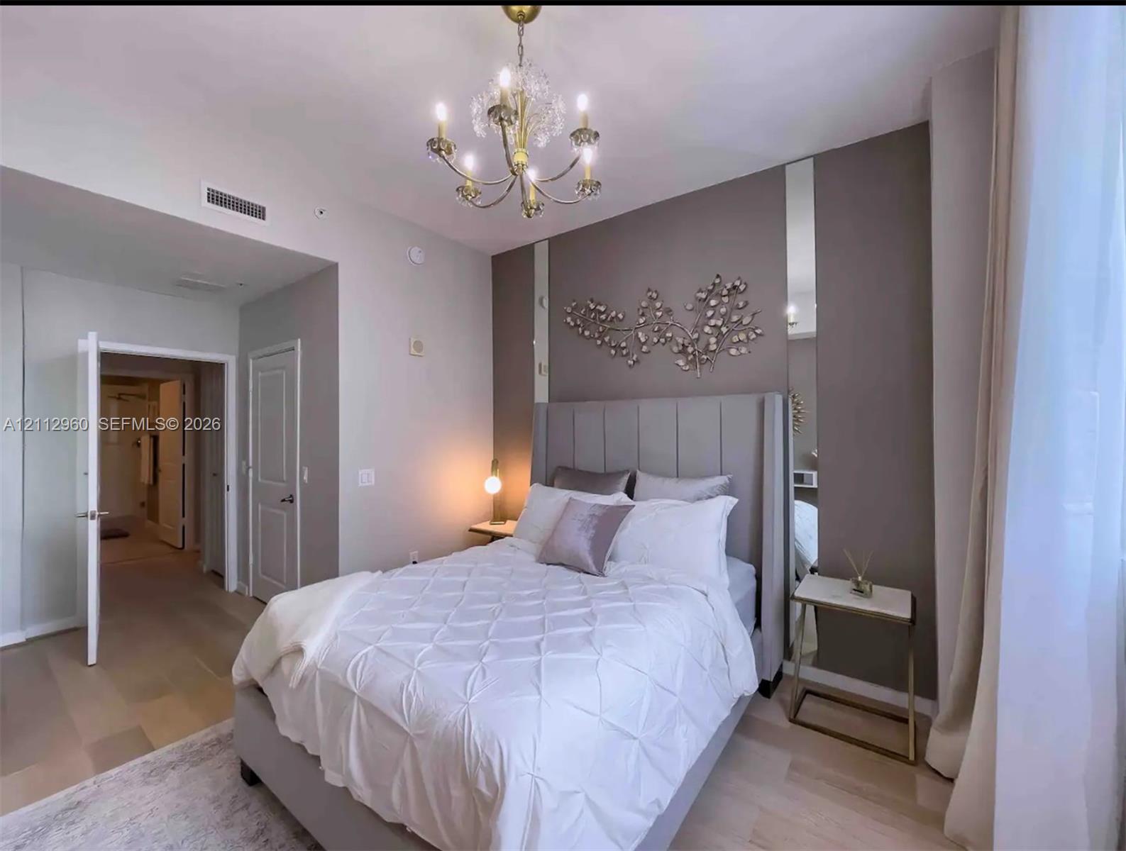 Multi-tone wall finish with vertical accent mirroring, multi-arm crystal chandelier, wood-finish flooring, and solid-core interior doors